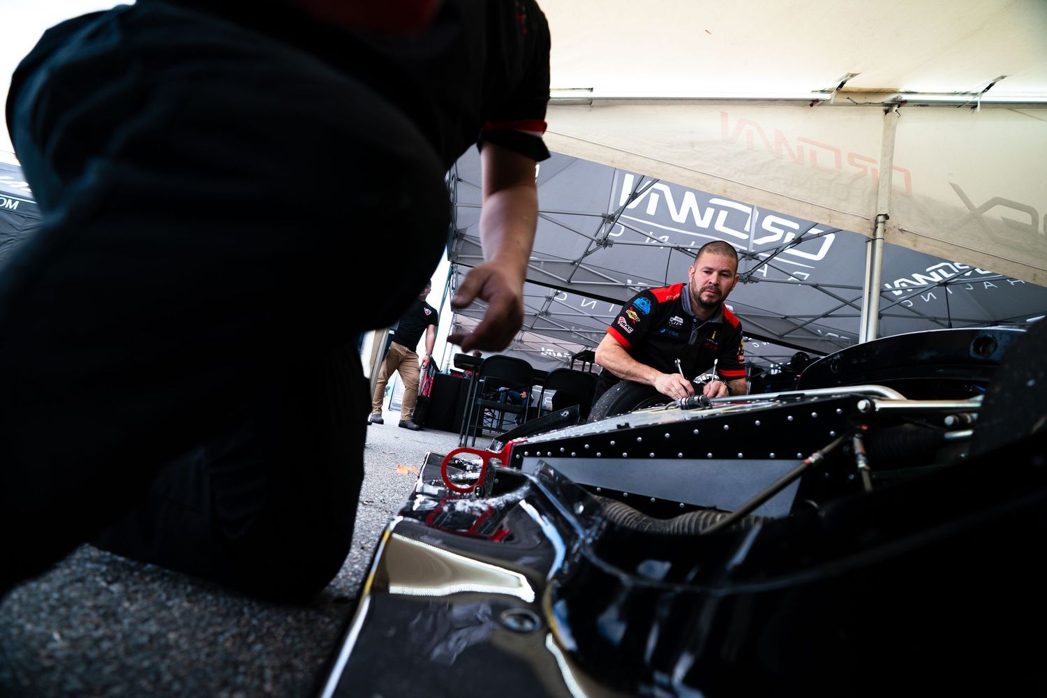 Racing team working on car adjustments in pit garage with technical equipment.