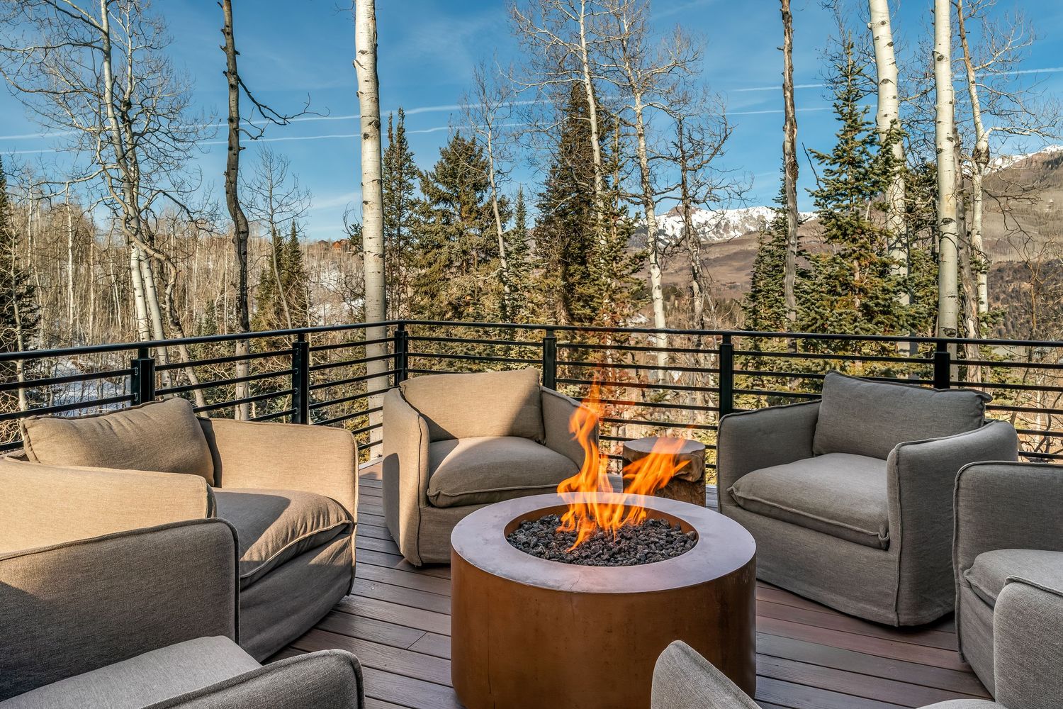 Outdoor deck seating area with fire pit and mountain views surrounded by snow-covered aspen trees.
