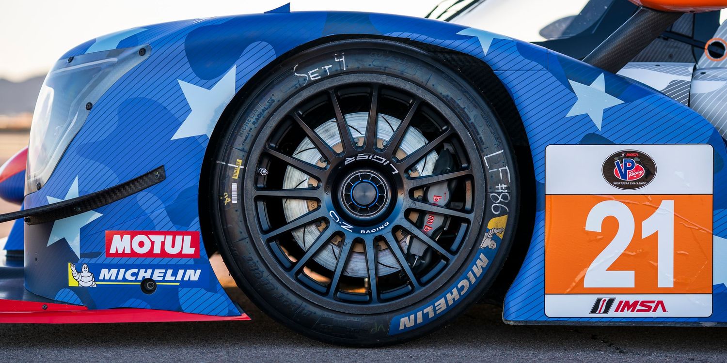 Racing car details showing blue bodywork, wheels, and technical components in bright sunlight.