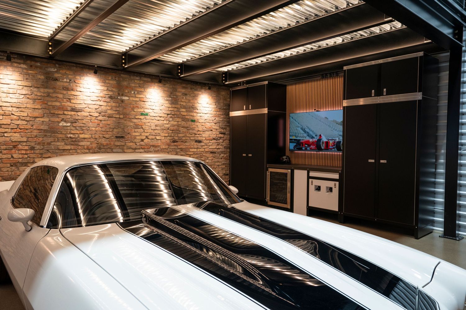 White classic car parked in luxury garage with exposed brick walls and modern entertainment system.