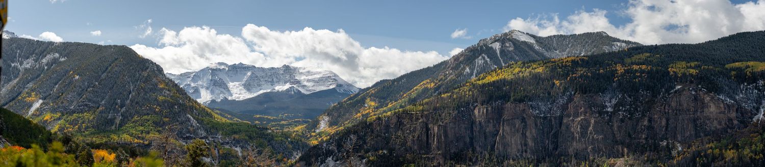 Panoramic mountain landscape with snow-capped peaks and dramatic rocky cliffs under blue skies.