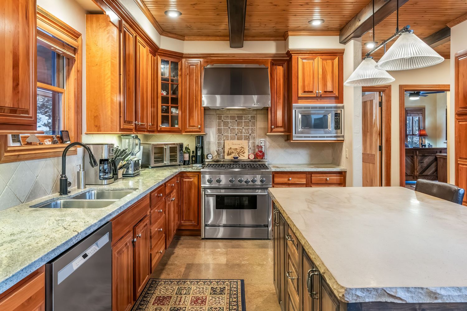 Luxurious kitchen with warm wood cabinets, granite countertops, stainless appliances and modern lighting fixtures.