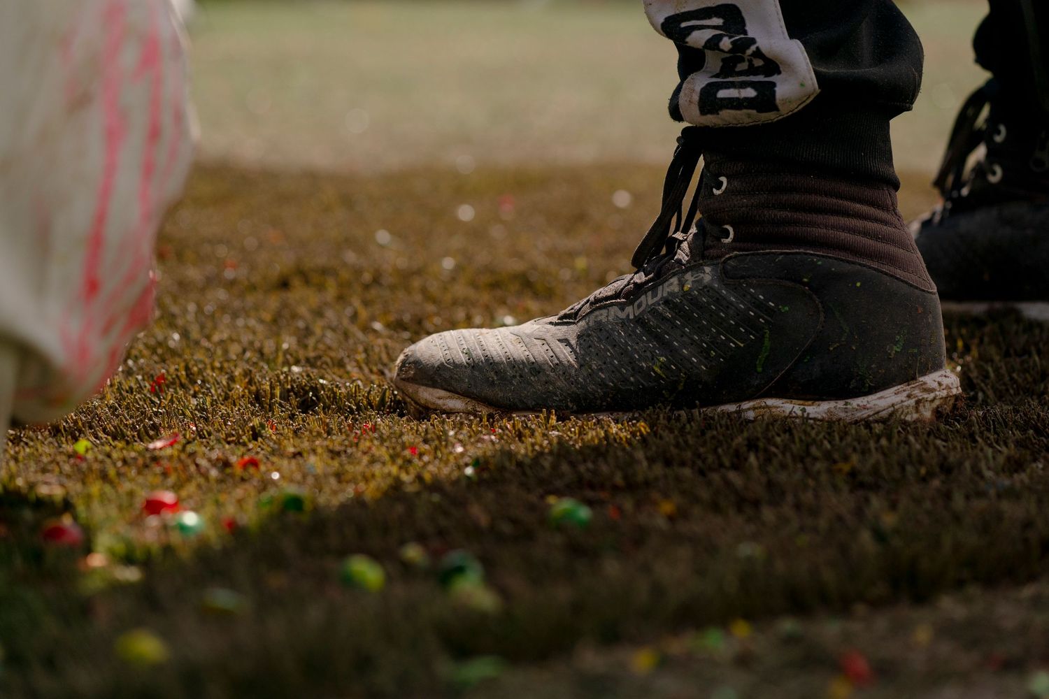 Close-up of tactical boots with paint splatter on grass during paintball game.