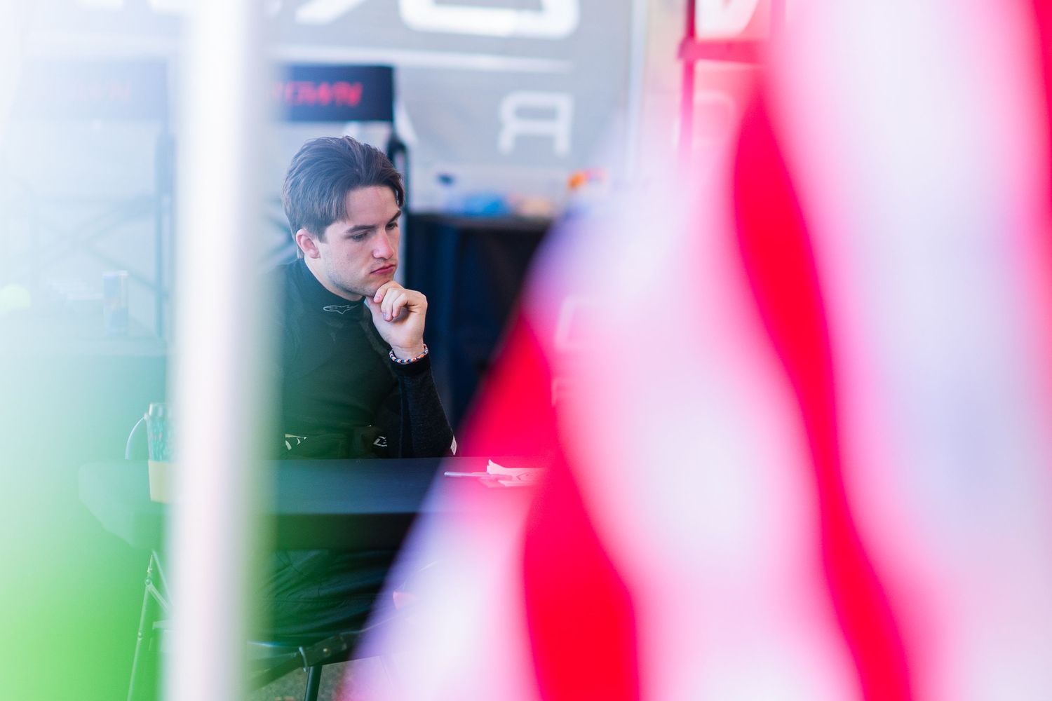 Person in green coat sits thoughtfully behind red and green blurred foreground elements in an artistic composition.