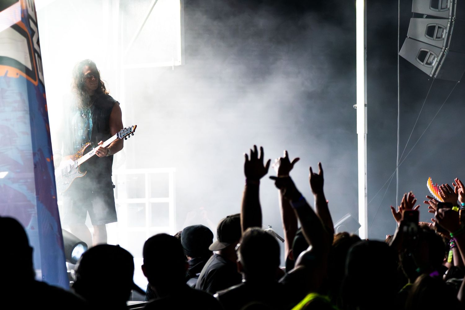 Silhouetted guitarist performs on a smoky stage before an energetic crowd throwing up rock hand signs.
