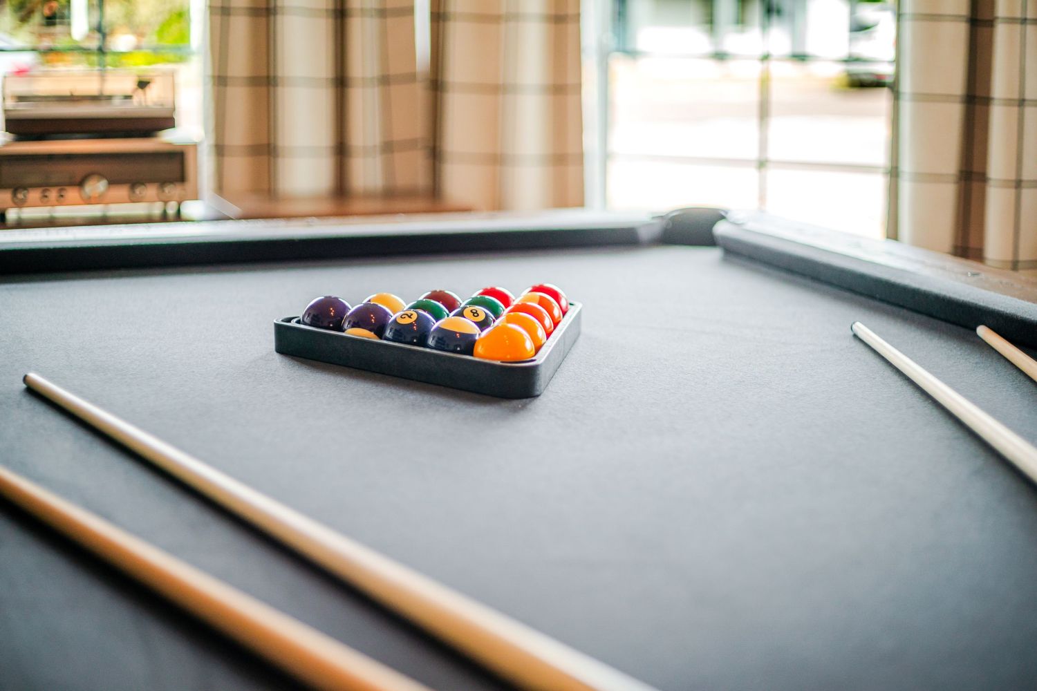 Pool table with wooden cue sticks and racked billiard balls on dark felt surface.