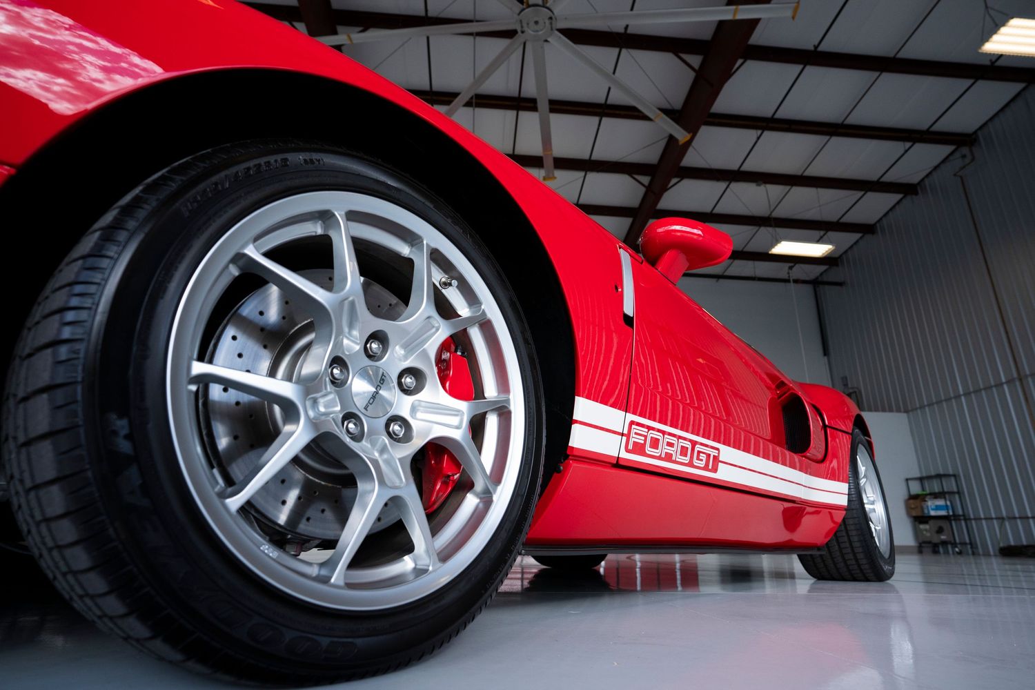 Low angle view of a red sports car wheel and brake system in a garage.