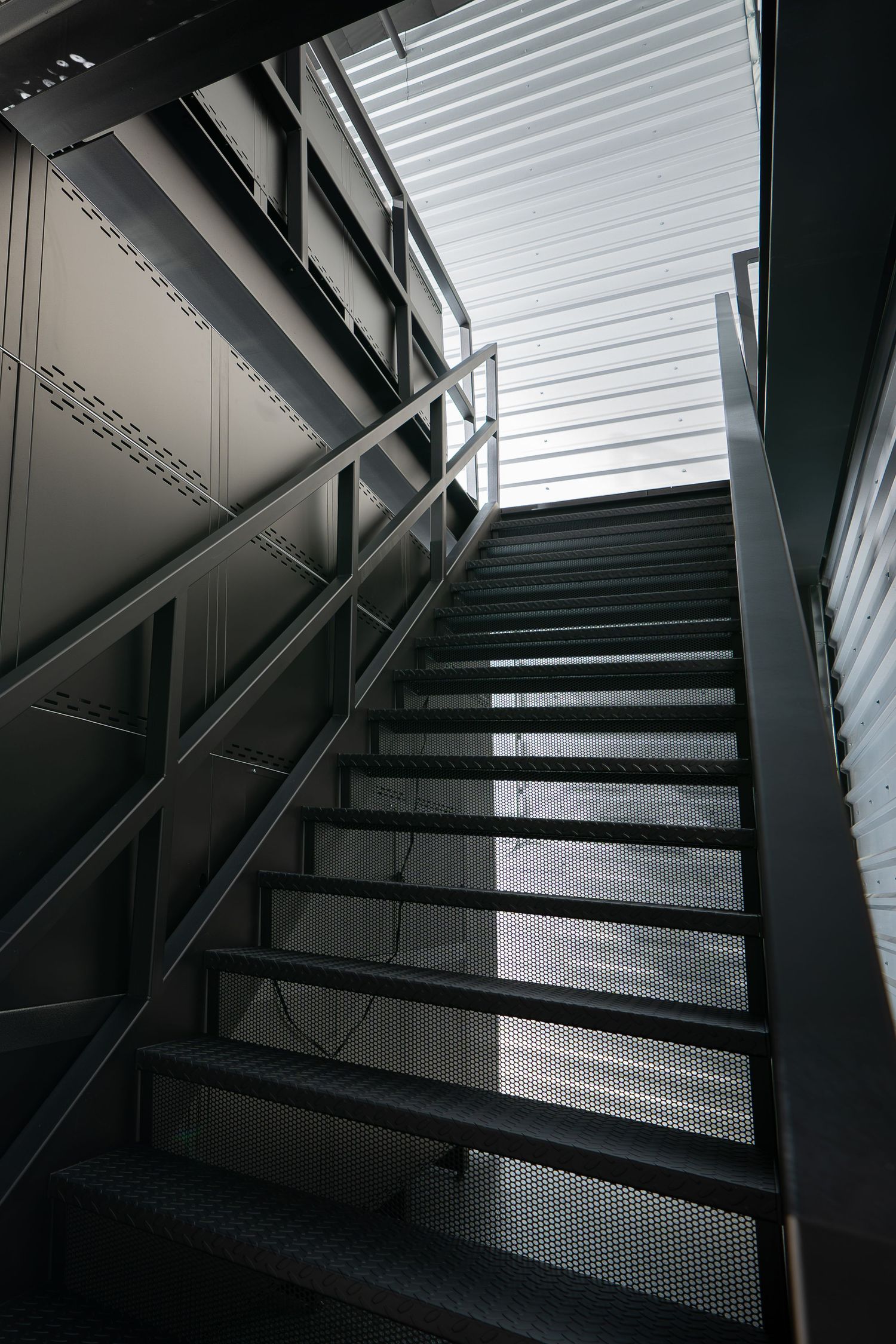 Industrial staircase with metal steps and black railings under geometric lighting patterns.