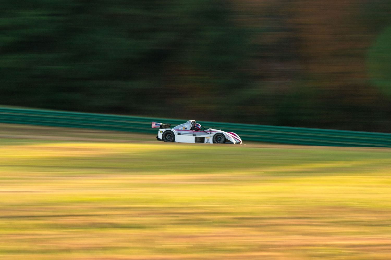 White race car photographed with motion blur effect against autumn-colored background.