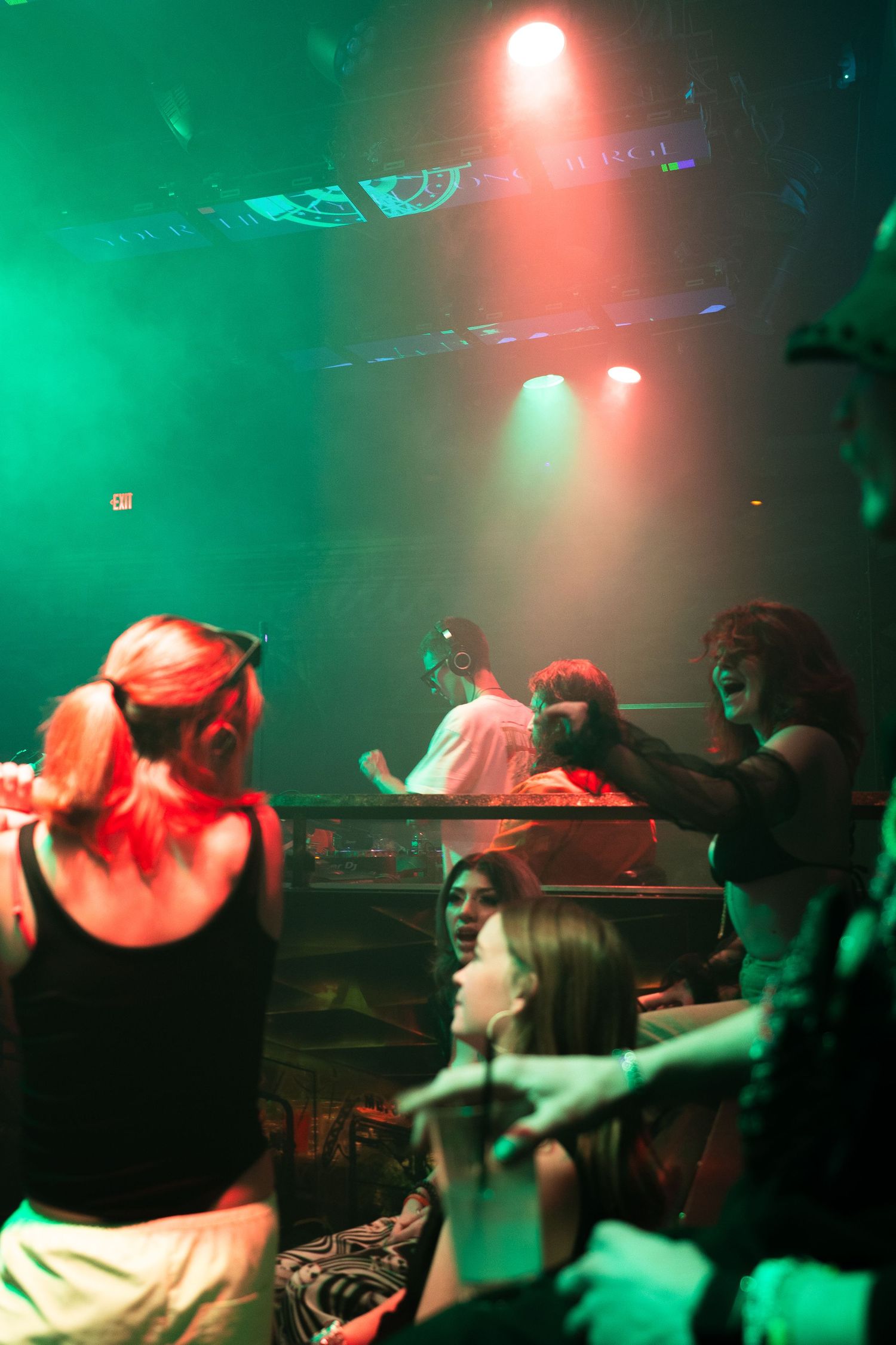 People dancing in a nightclub under red and green lighting with a smoky atmosphere.