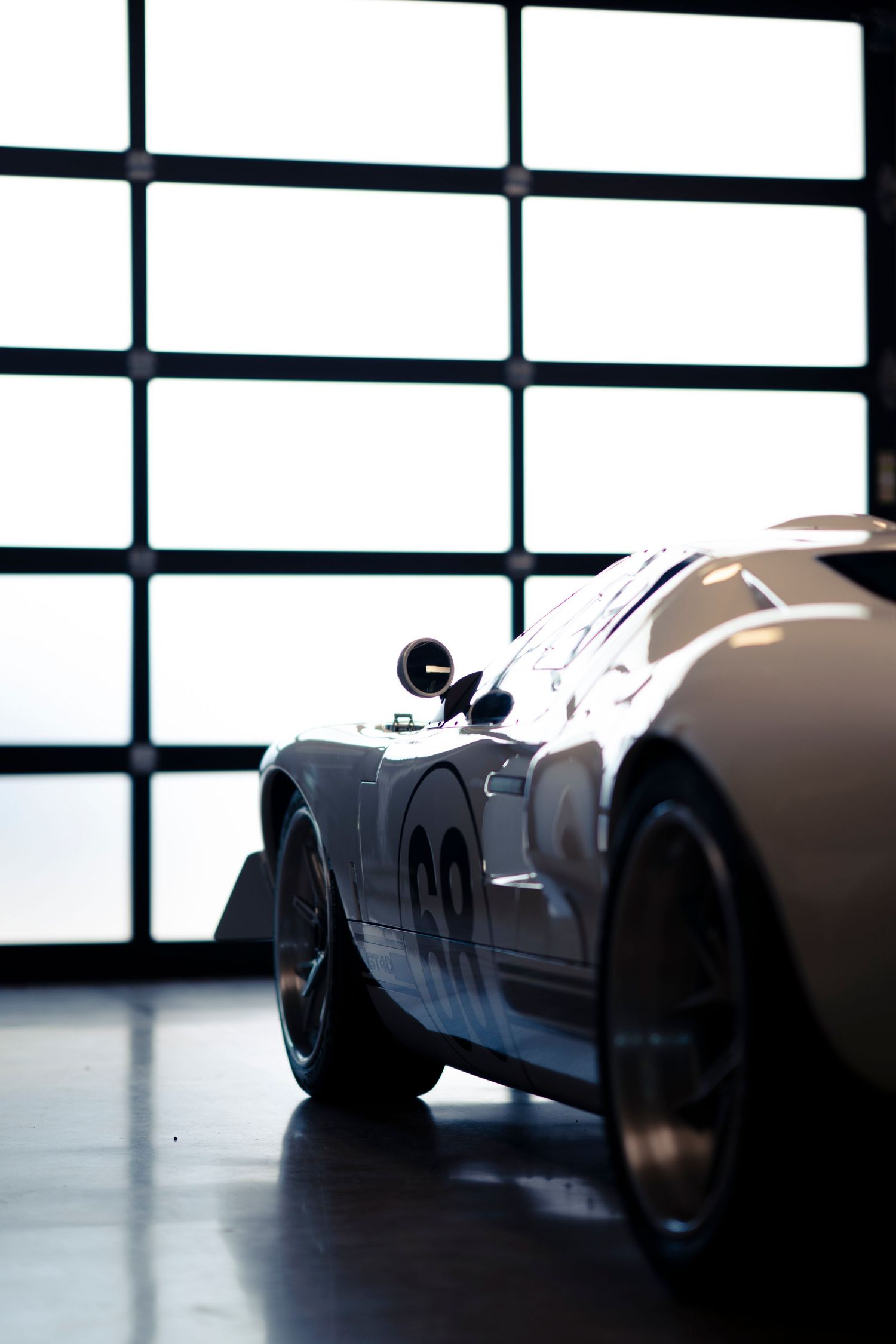 A sleek silver vintage sports car photographed in dramatic lighting against a white modern interior background.