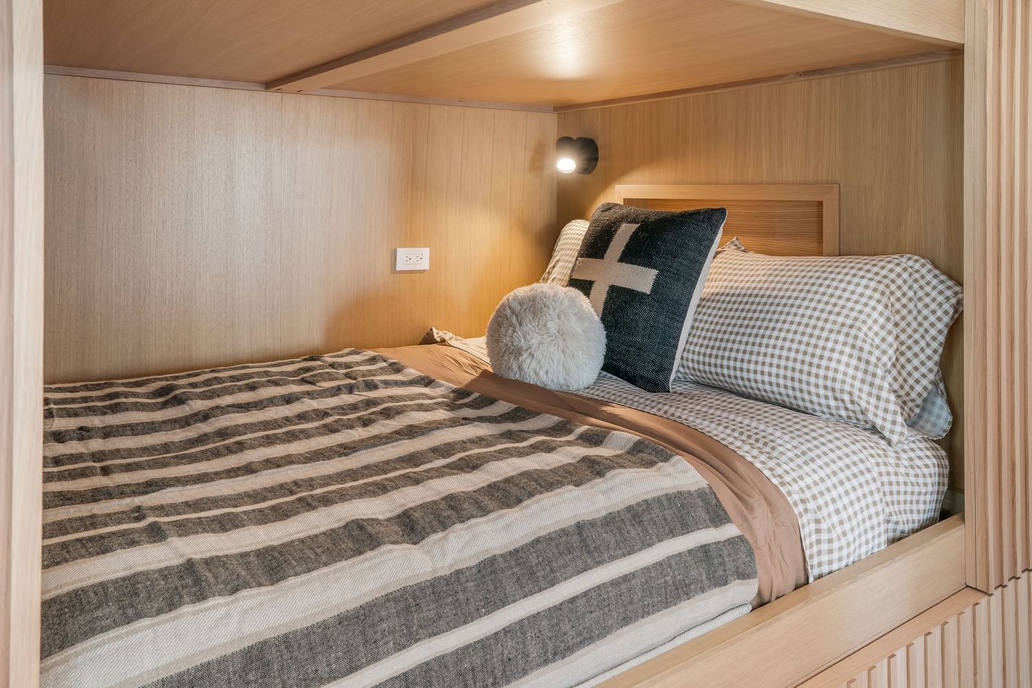 Modern tiny house interior showing a built-in sleeping loft with wooden paneling and recessed lighting.