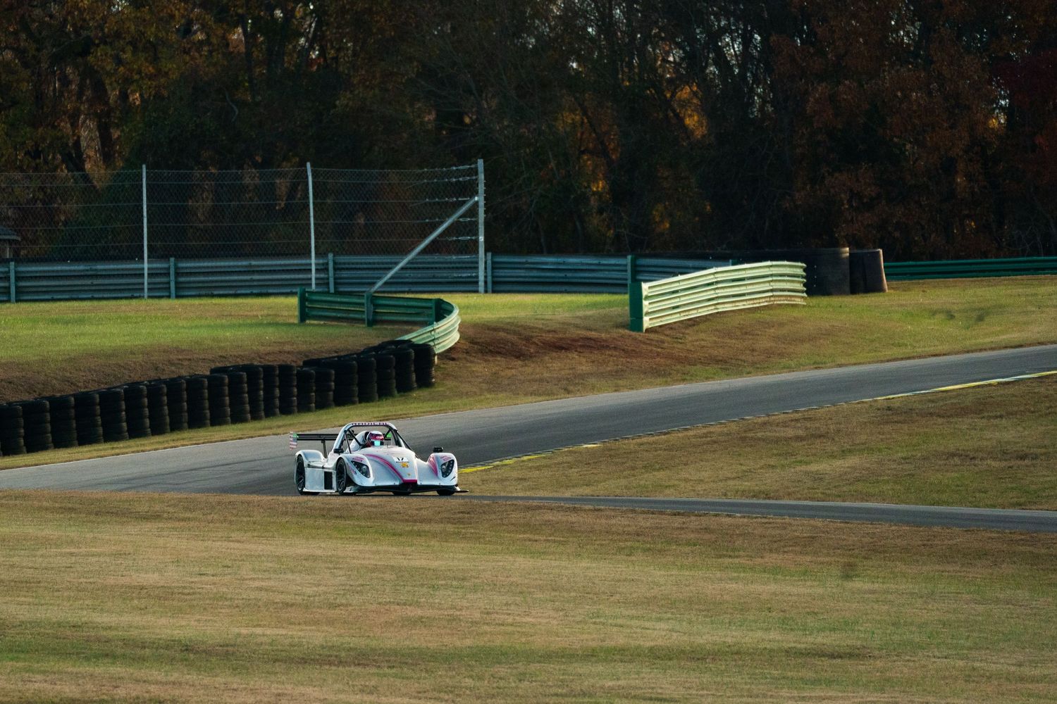 White Formula 1 car races along an empty track with autumn trees in the background.