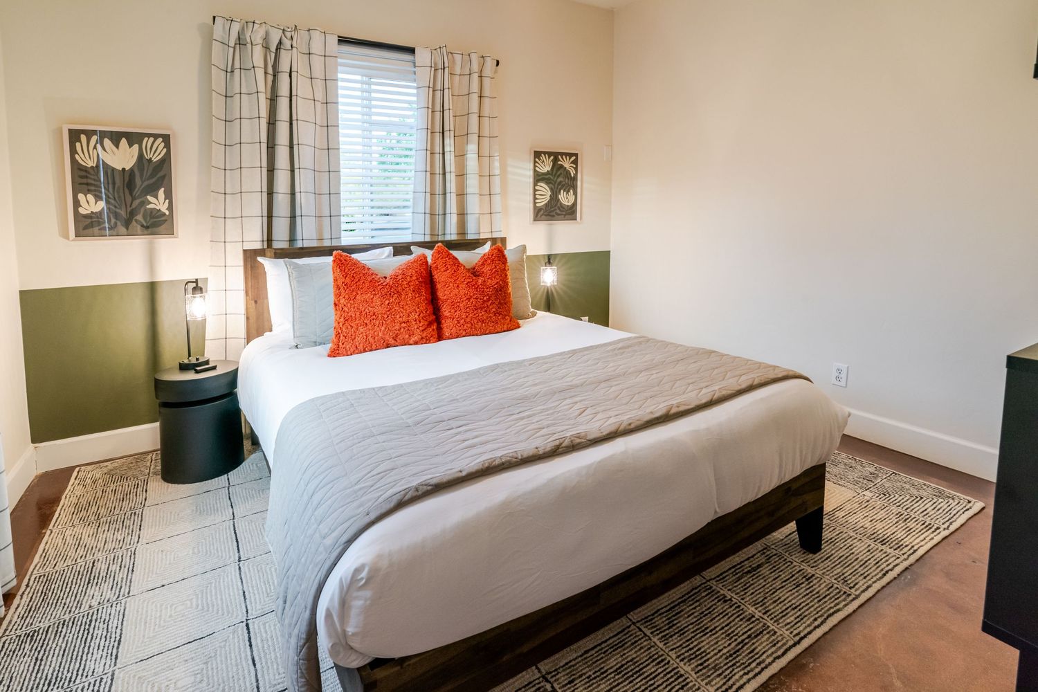 Contemporary bedroom with orange pillows, plaid curtains, and green accent wall behind white bedding.