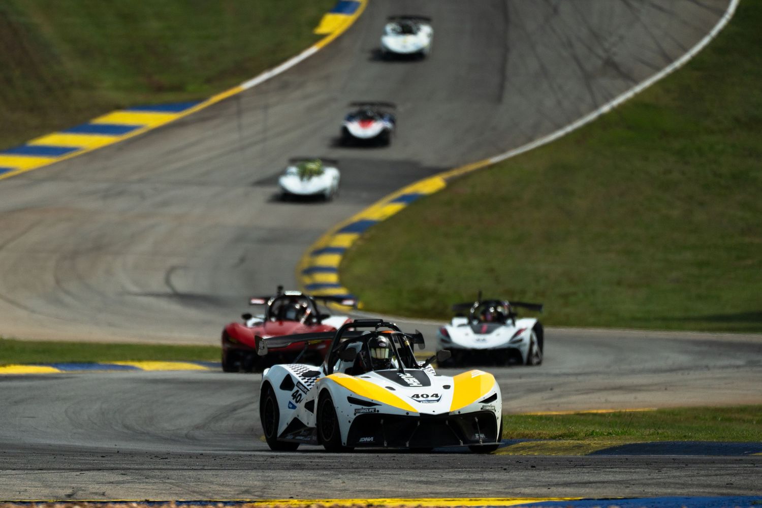 Open-wheel race cars navigate a winding road course during a competitive motorsport event.