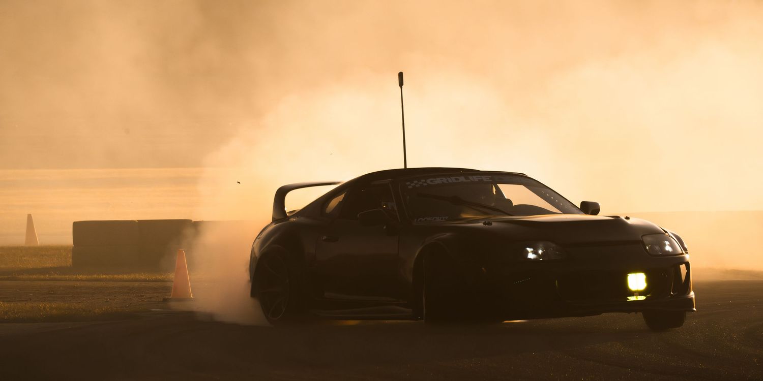 Black sports car drifting on a track at sunset, surrounded by dramatic smoke clouds in golden light.