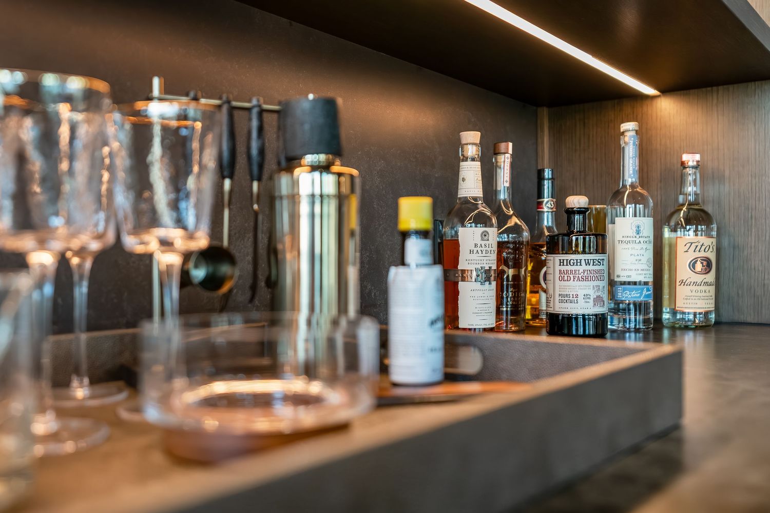 Elegant home bar setup with collection of spirits and glassware on dark shelving.