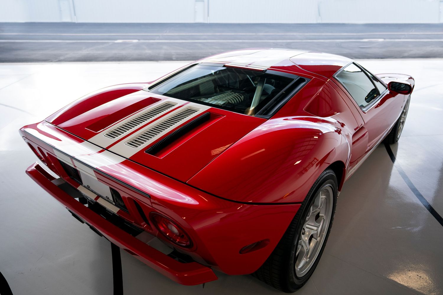 Rear view of a red sports car with racing stripes in a white showroom.