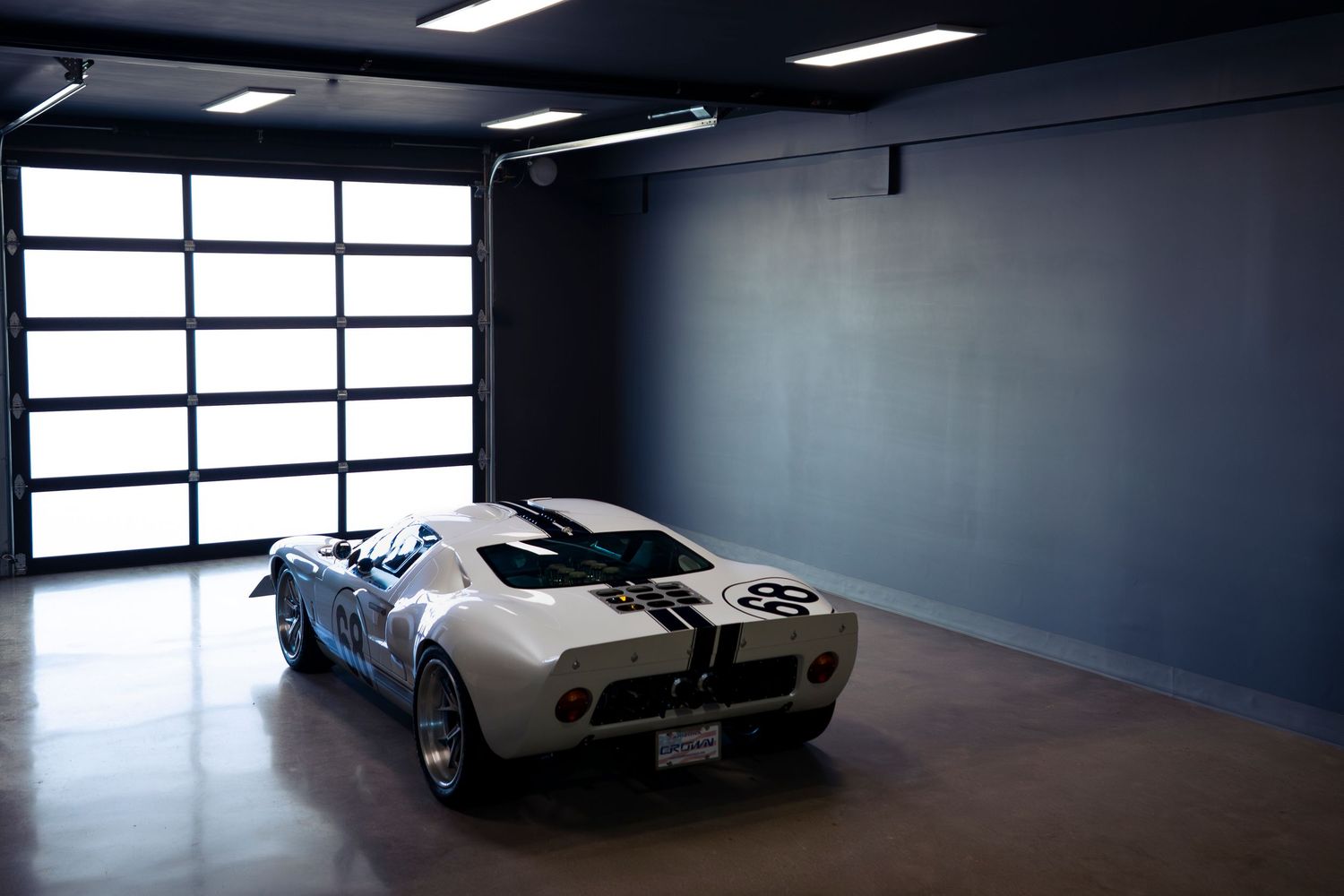 A sleek silver sports car sits in a modern showroom with large windows and dramatic lighting.