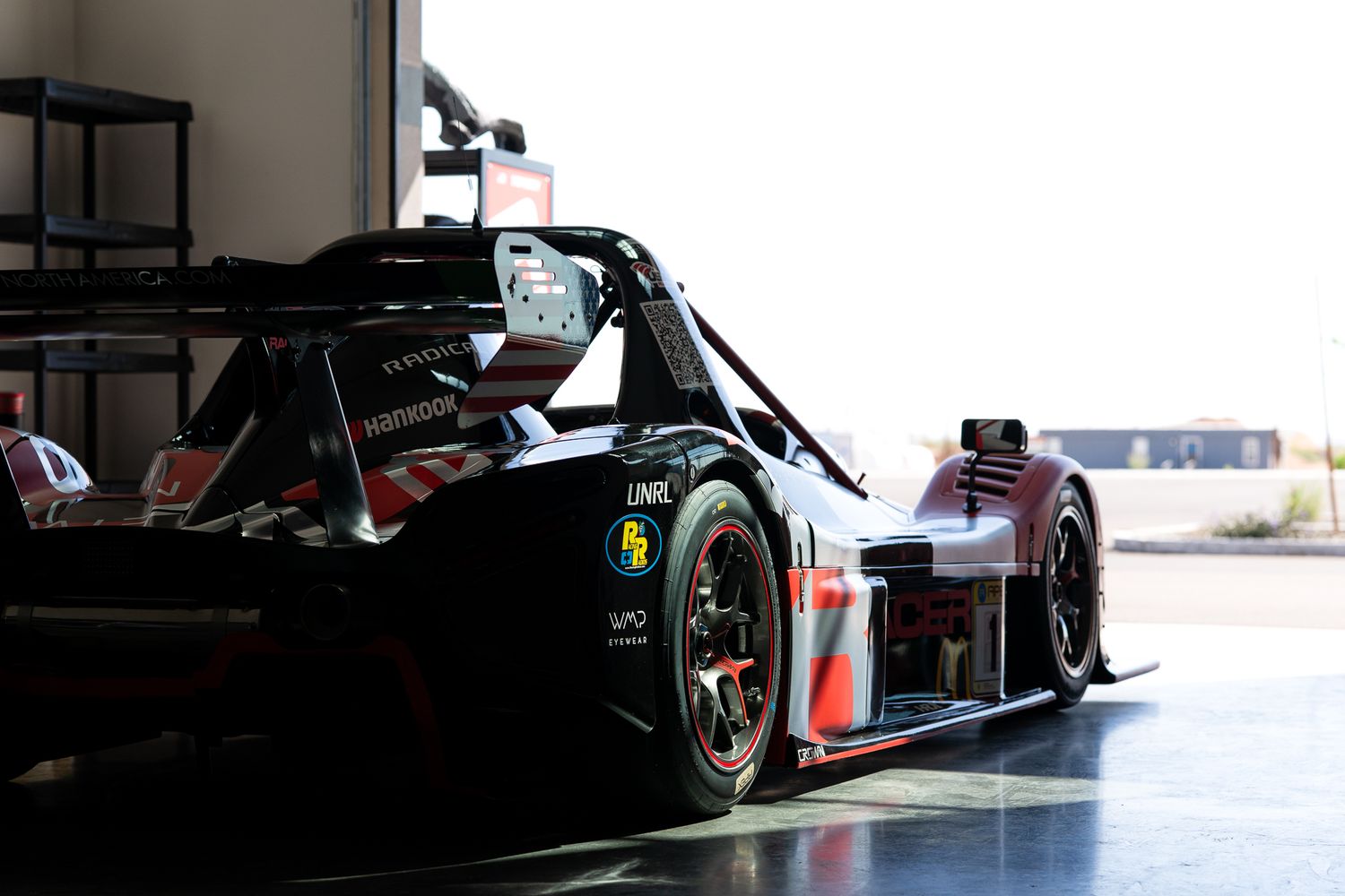 Formula 1 cars lined up in pit lane with mechanics and equipment visible in the background.