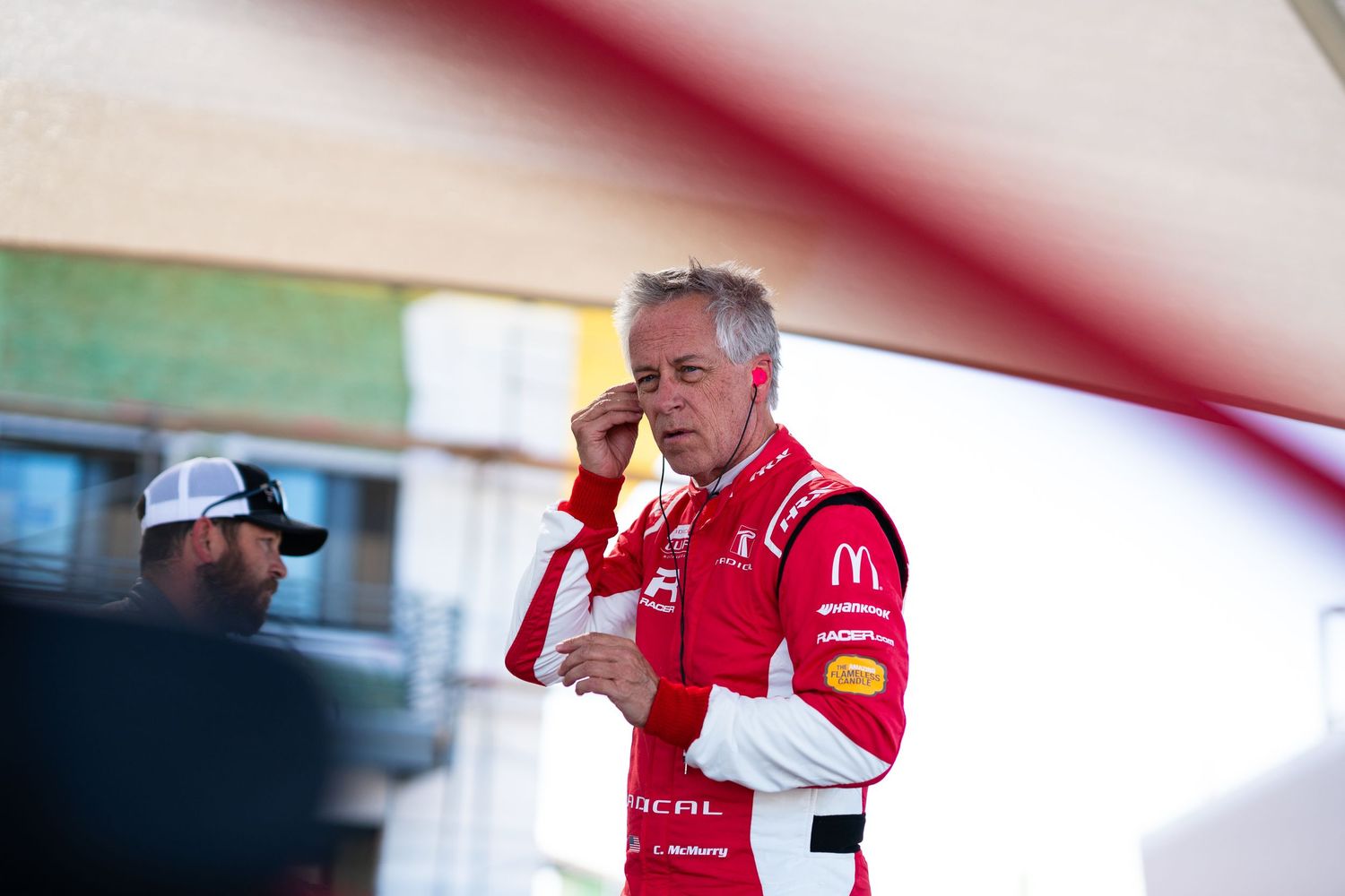 Driver in red racing suit makes final preparations in cockpit of race car.