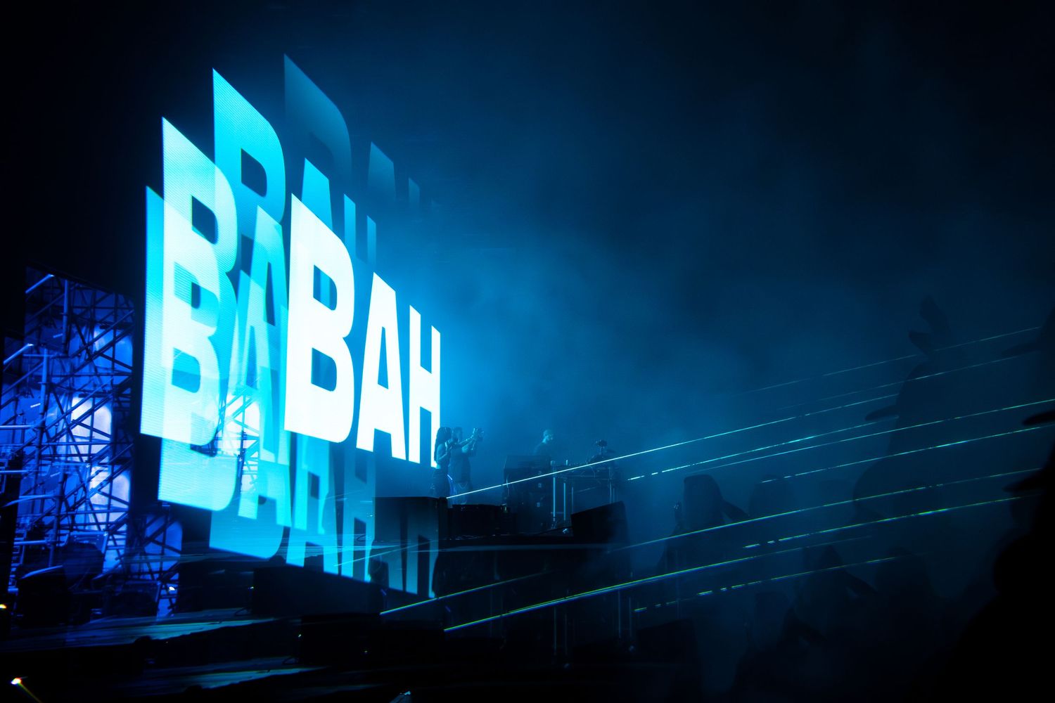 Blue illuminated BABAH sign on stage at a concert with dramatic lighting and fog effects.