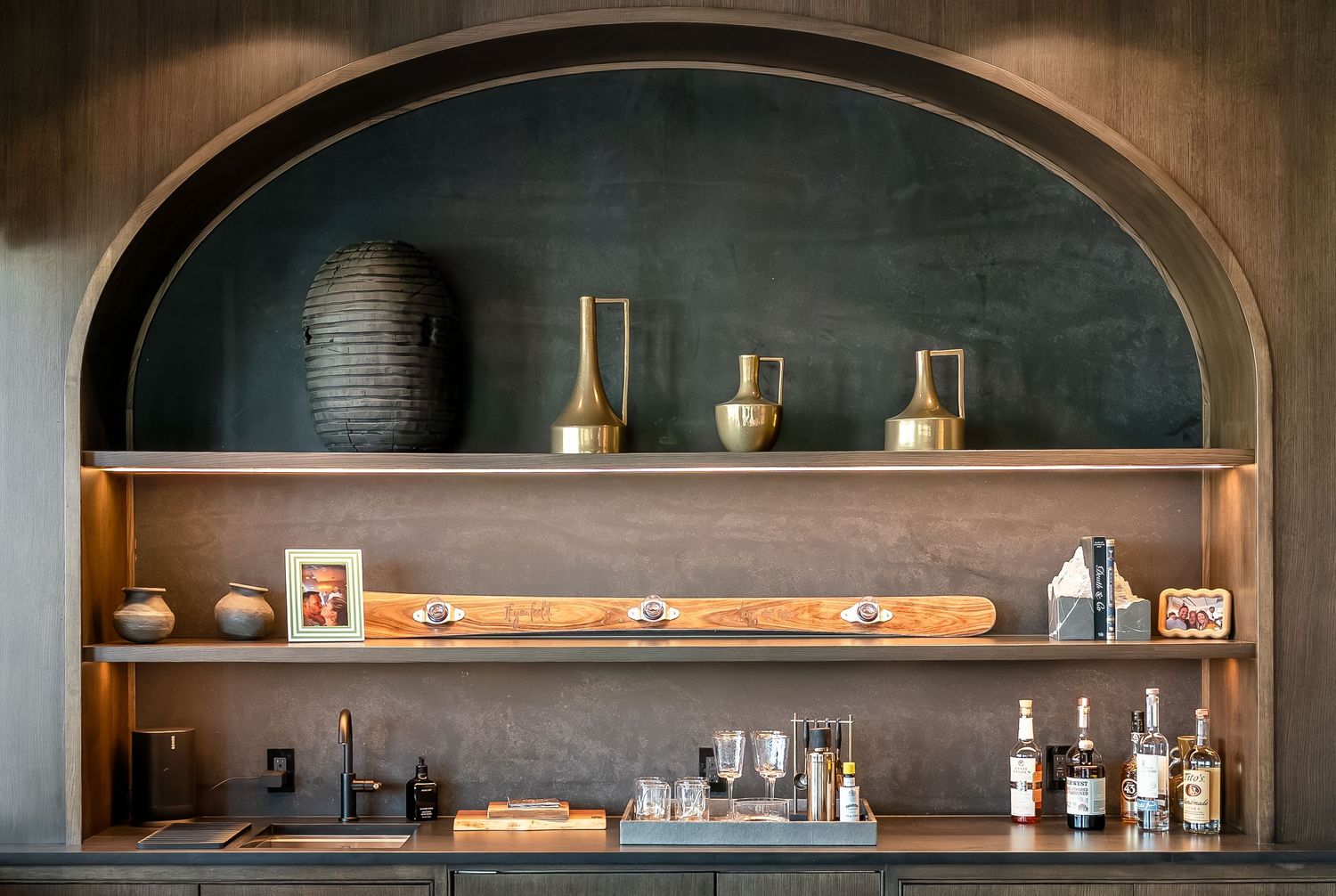 Dark wood shelving with arched design displays decorative items against a moody wall backdrop.