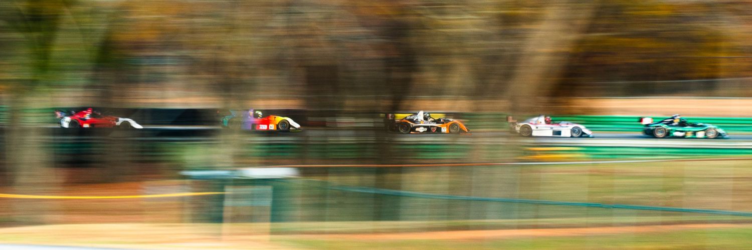 Motion-blurred shot of multiple race cars competing on track during a motorsport event.