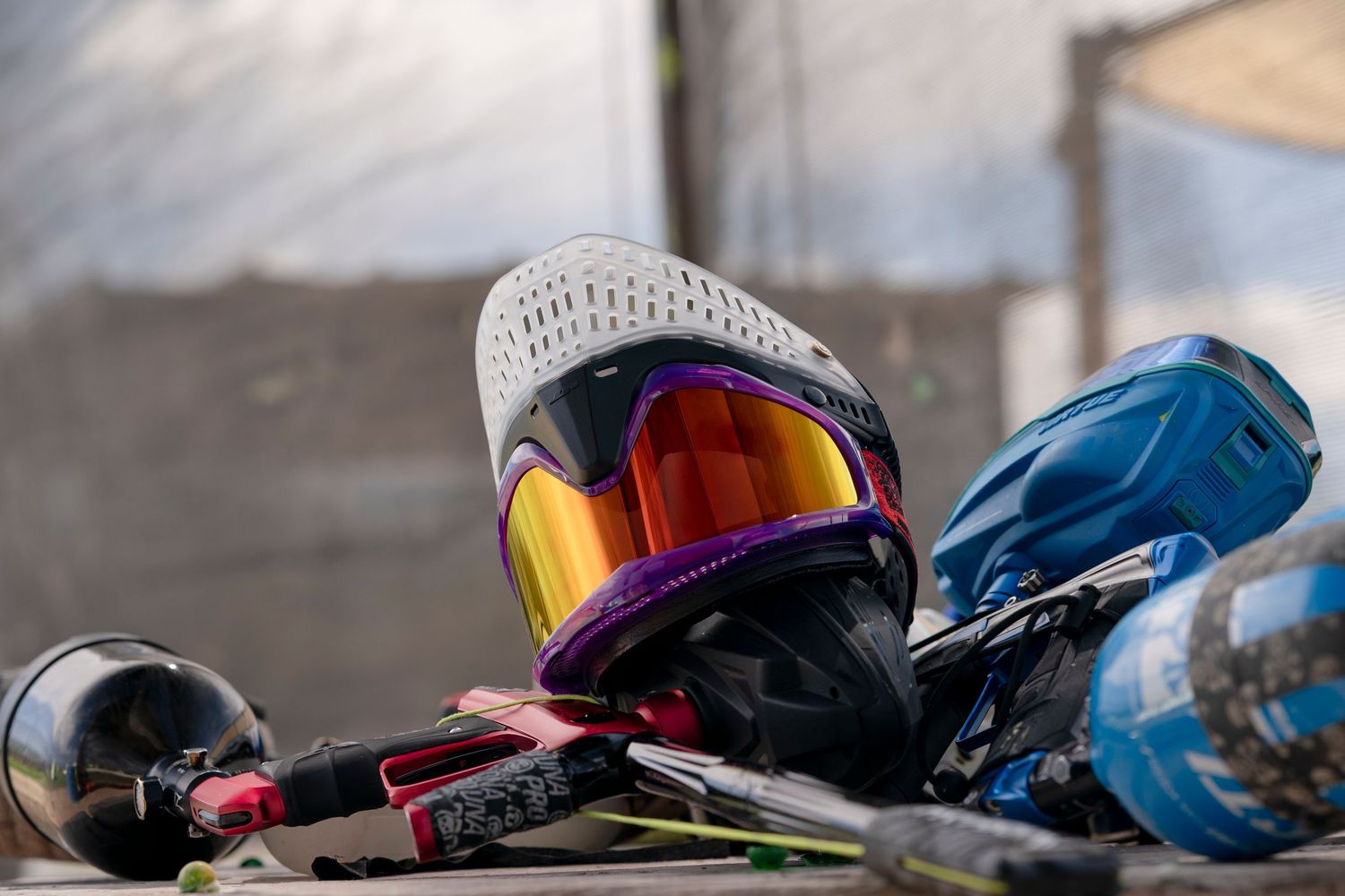 Close-up of paintball mask with orange reflective lens and equipment.