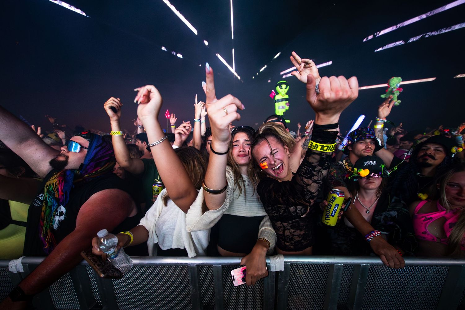 Excited festival crowd cheering at a music concert with colorful lights and glow sticks at night.