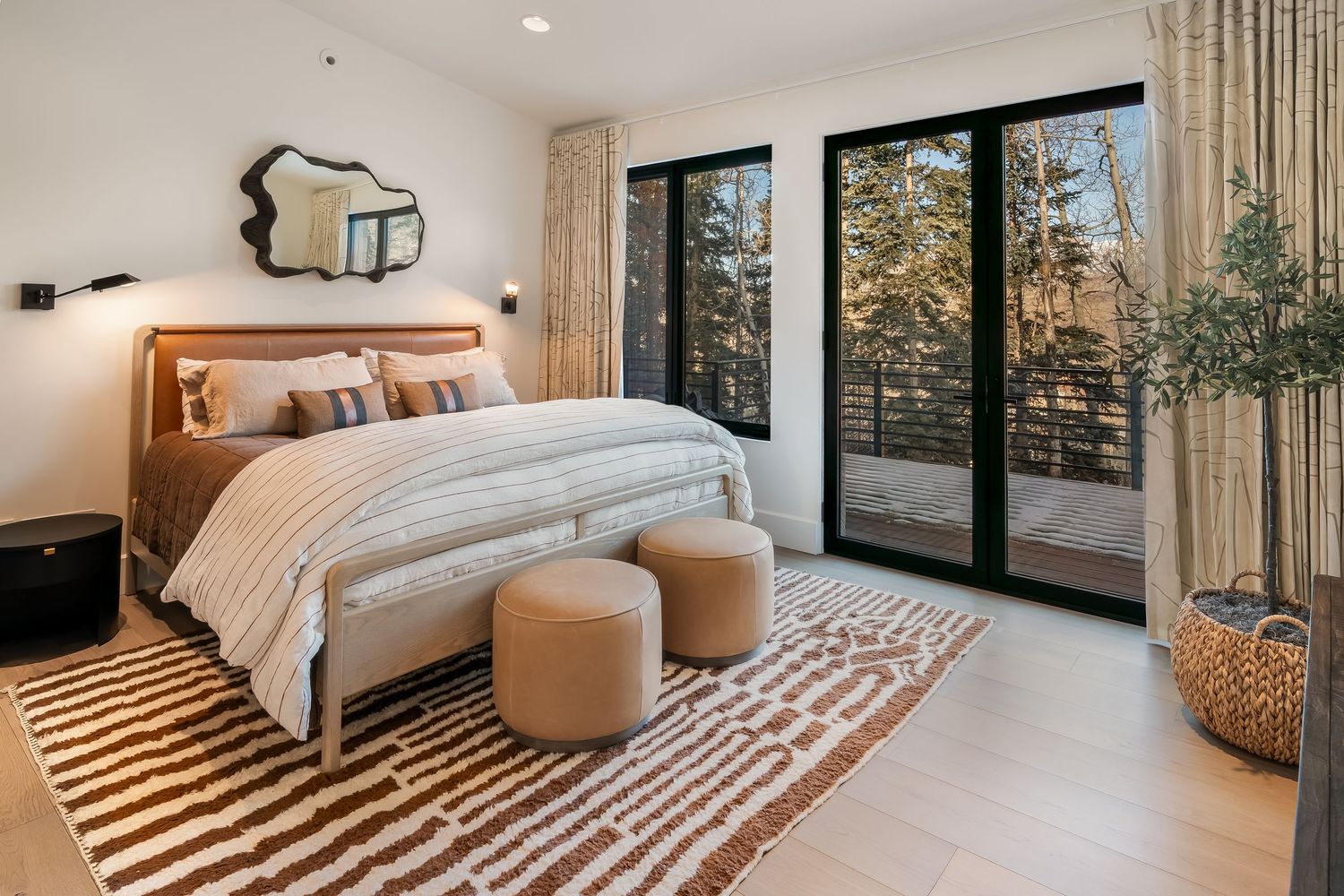 Modern bedroom with sliding glass doors features neutral decor, geometric patterns, and mountain views through large windows.