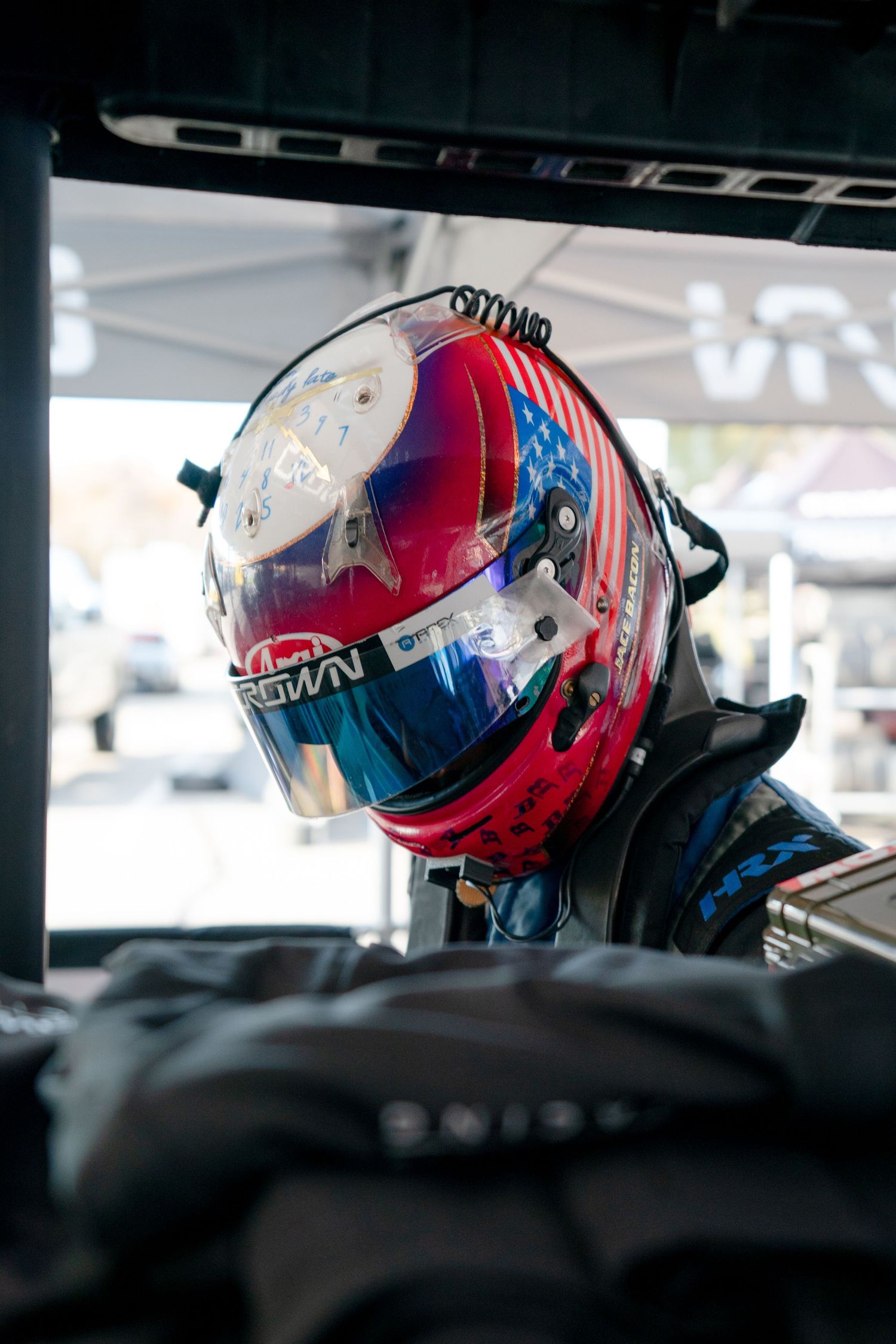 Red and blue racing helmet with reflective visor sits mounted inside race car cockpit.
