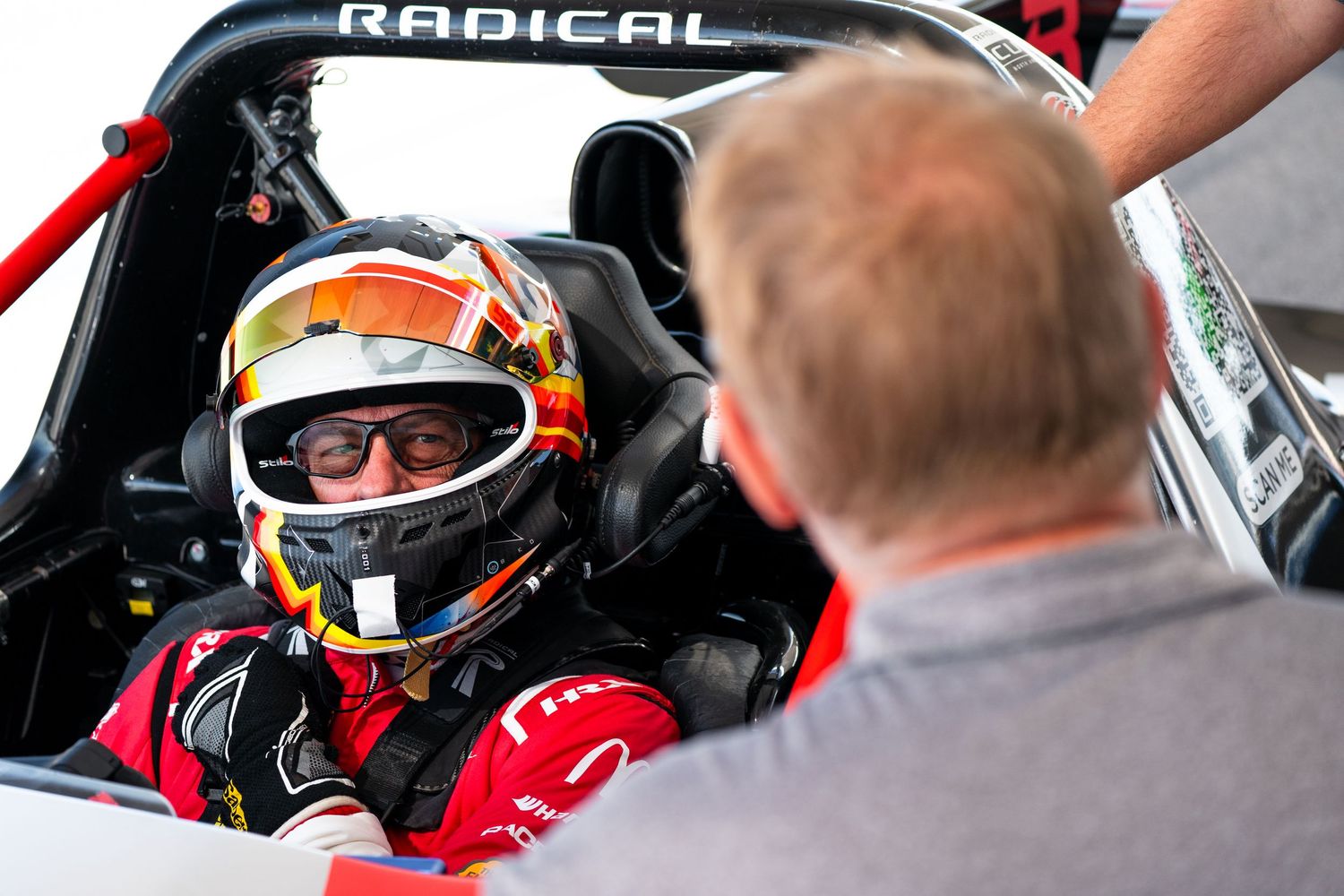 Close-up view of racing car cockpit with Radical branding visible during driver preparation.
