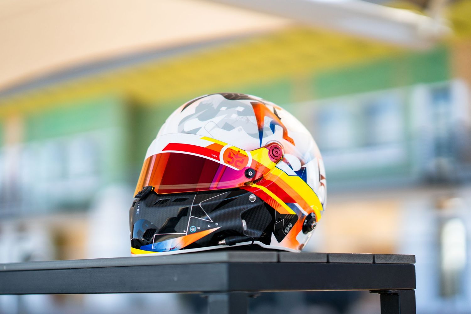 Racing helmet with orange and red accents sits on display at motorsport event.