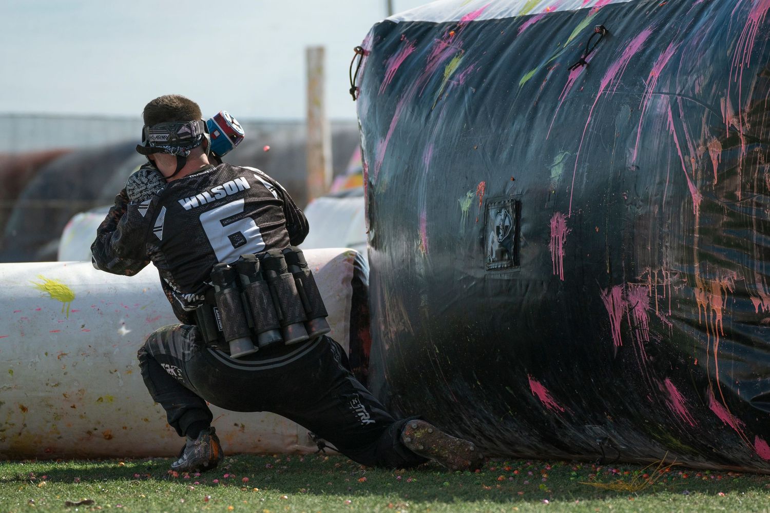 A paintball player takes cover behind inflatable bunkers with pink splatter marks during a competitive match.