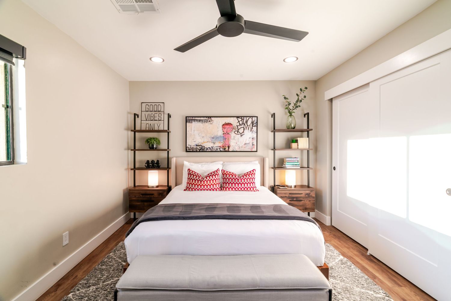 Bright master bedroom with modern decor, red accent pillows, and ceiling fan.