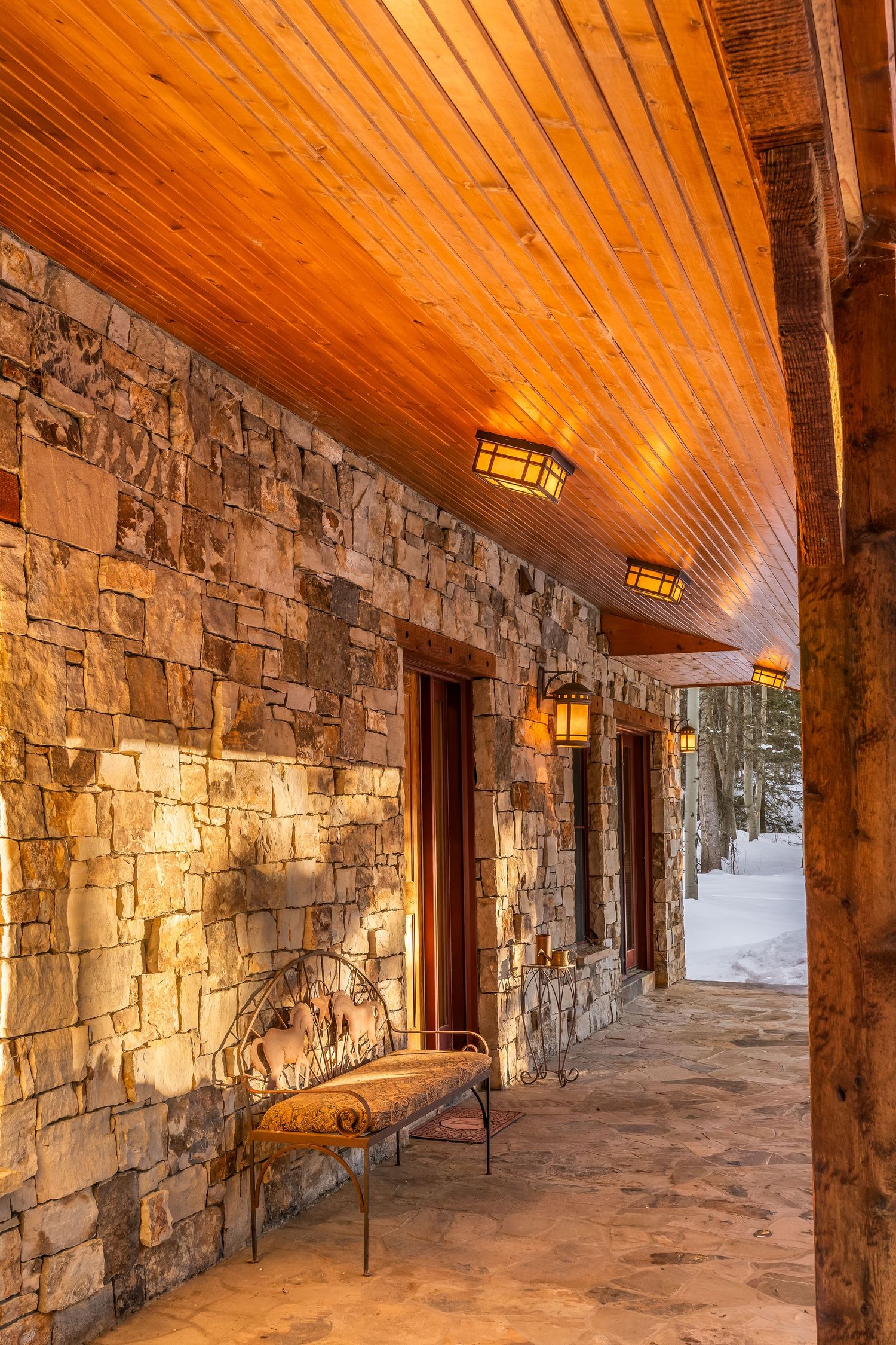 Rustic stone wall corridor with wooden ceiling, lantern lights and decorative bench creating a cozy mountain lodge ambiance.