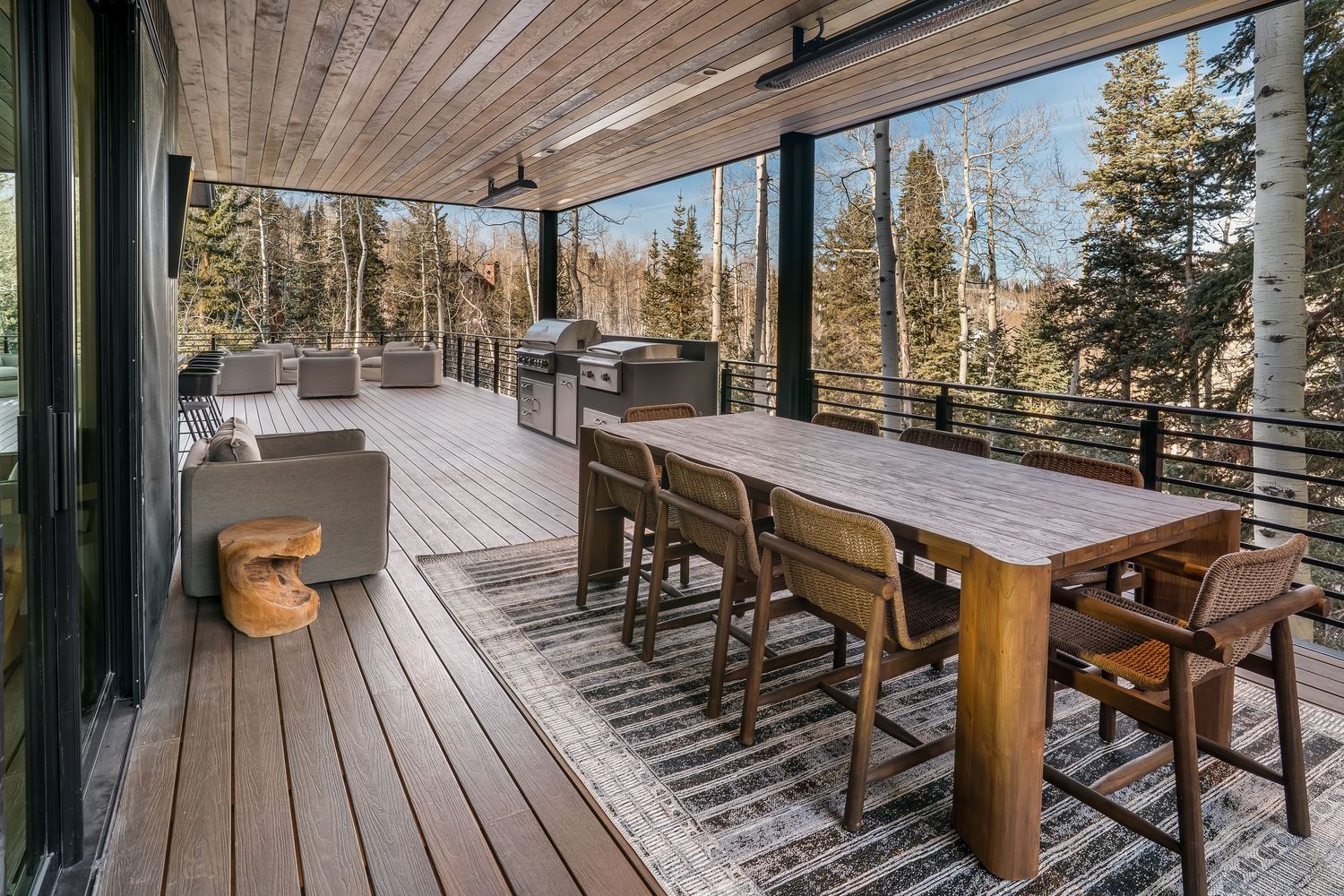 Spacious mountain deck with wooden dining table and chairs overlooking forest landscape.