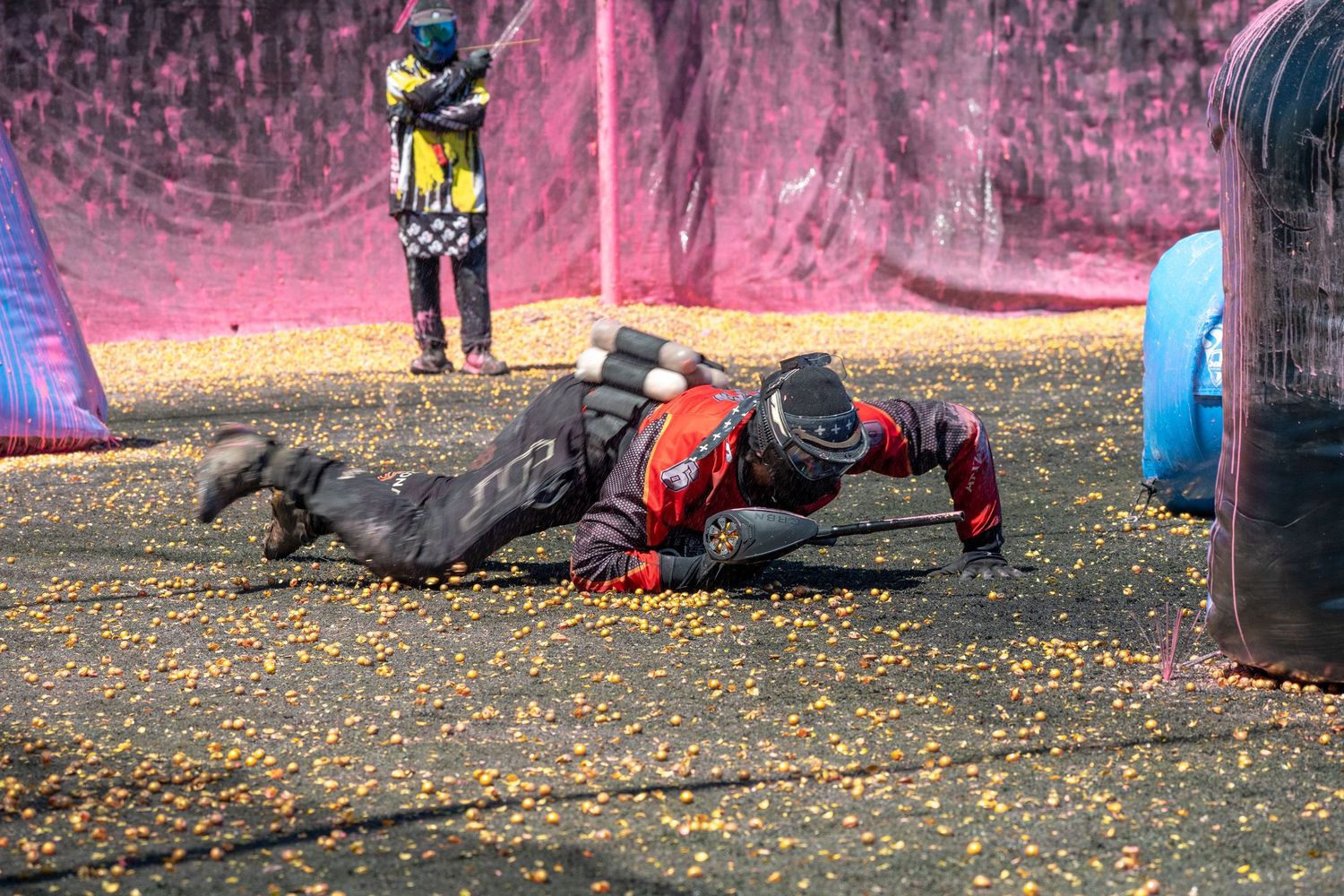 Paintball player in red uniform lying prone on ground during competitive paintball match.