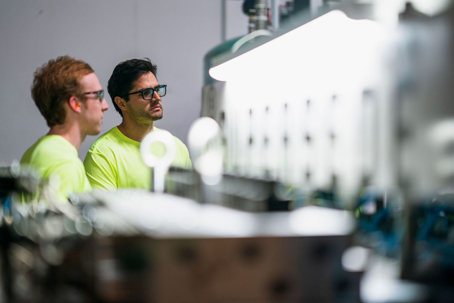 Workers in bright safety gear monitoring production equipment in a manufacturing facility.