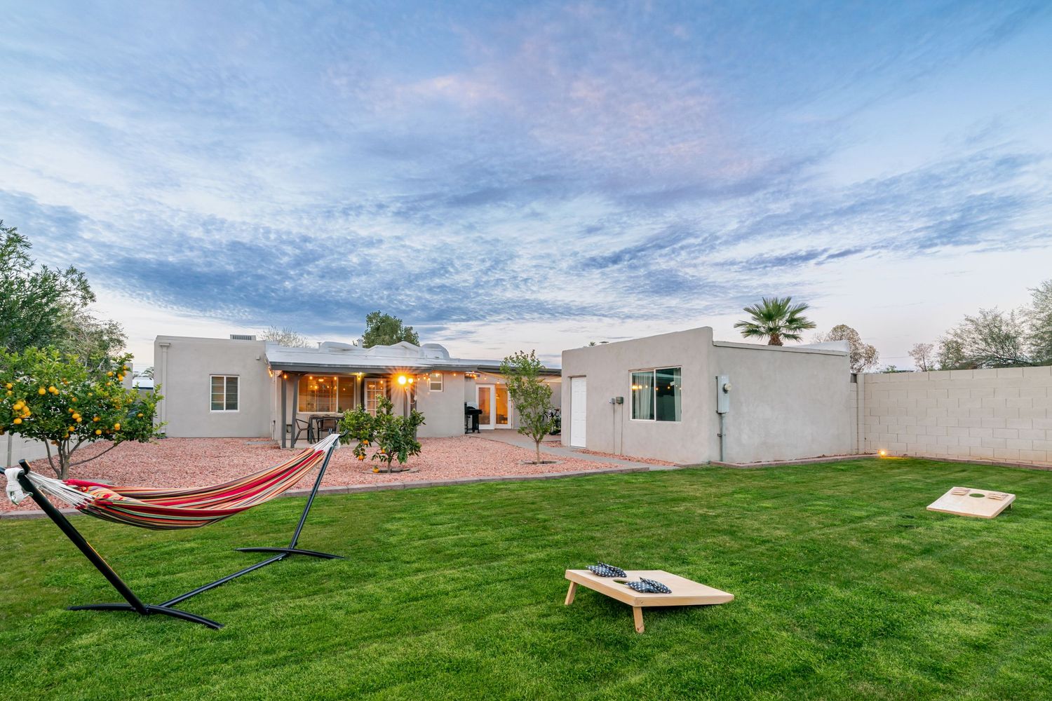 Spacious backyard with green lawn, hammock, and lounge chairs under blue sky.