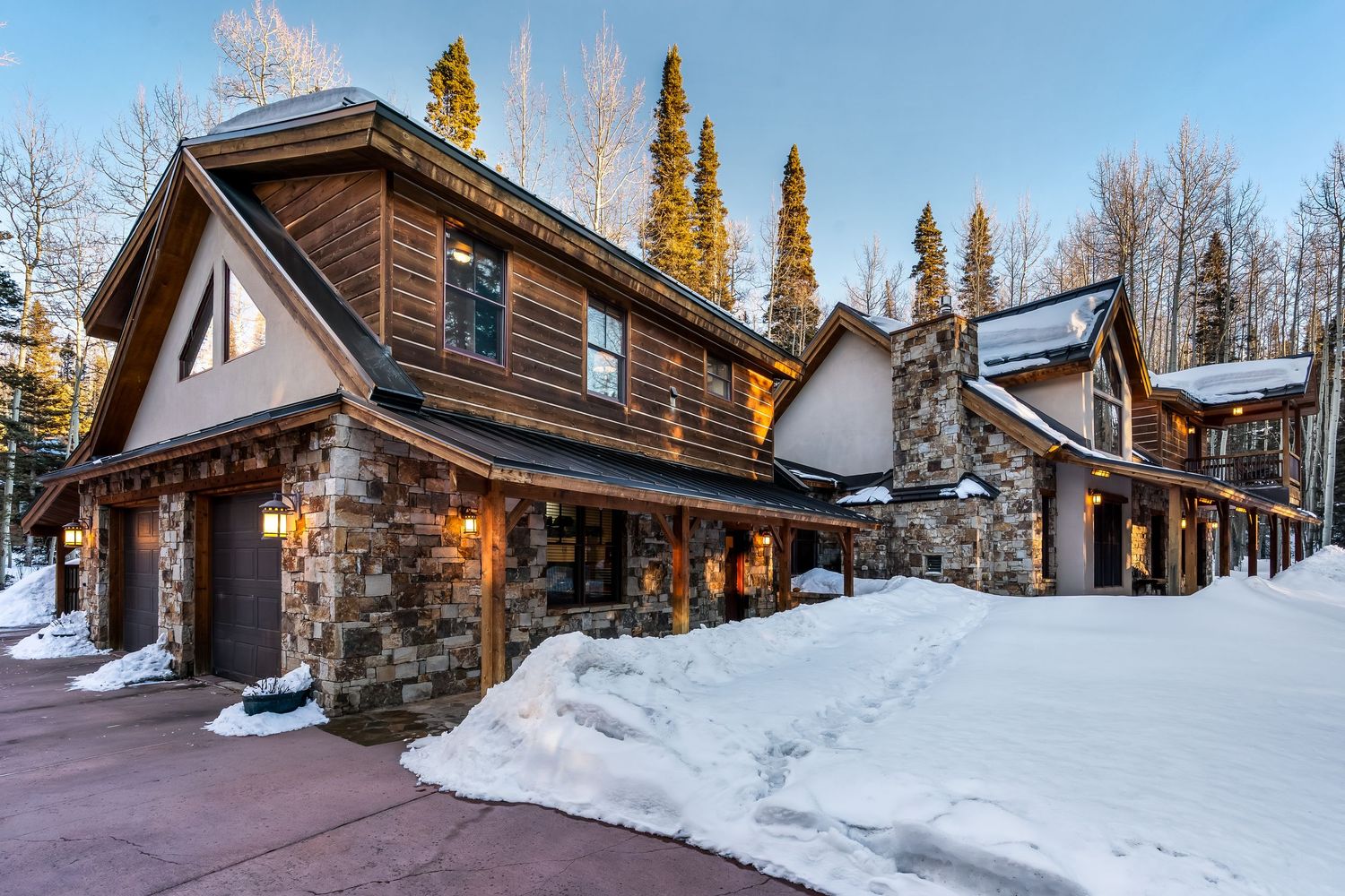 Snow-covered luxury mountain lodge exterior with tall pine trees and dramatic winter landscape views.