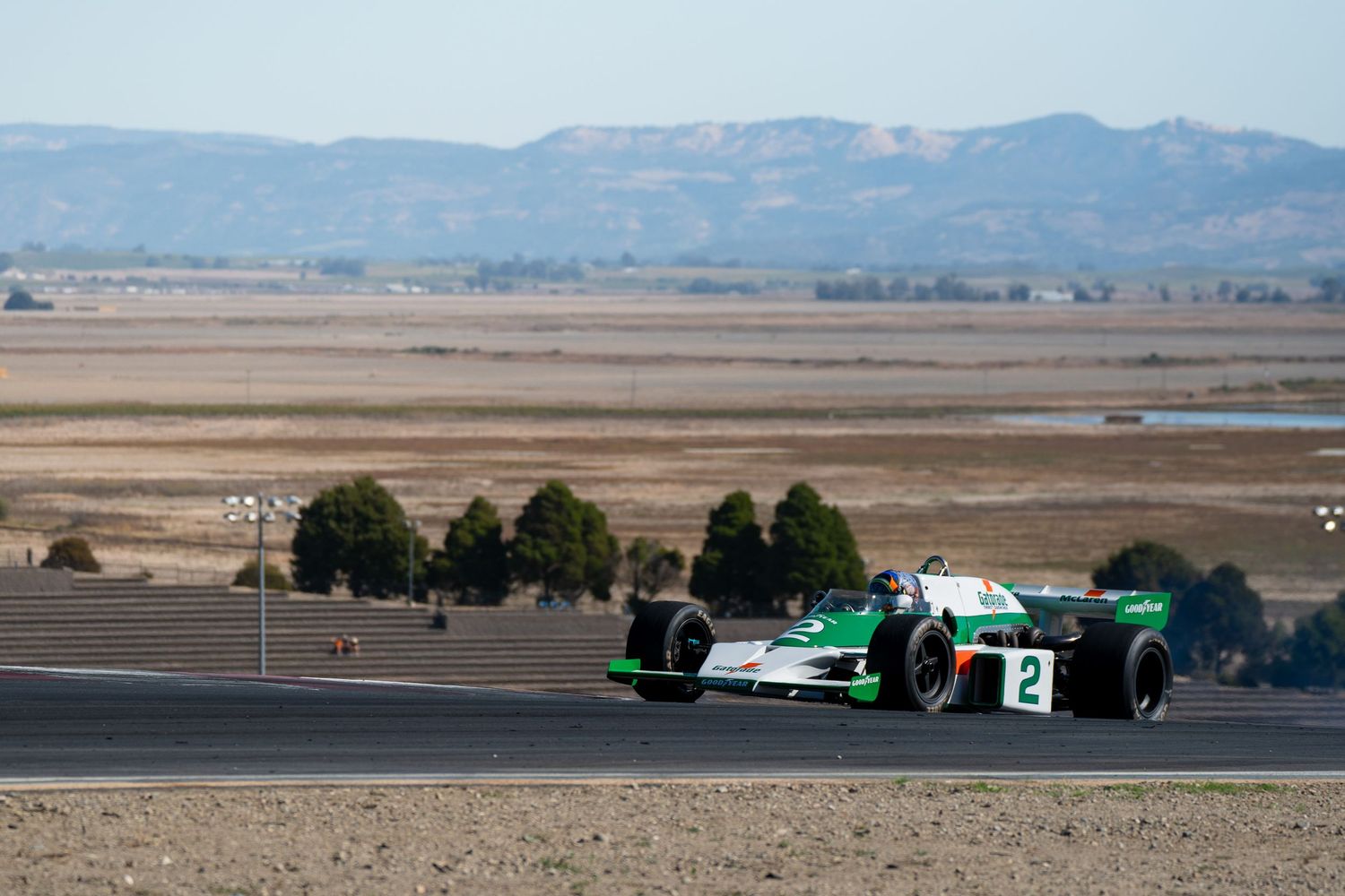Race car speeds along a desert track with mountains in the background during a motorsport competition.