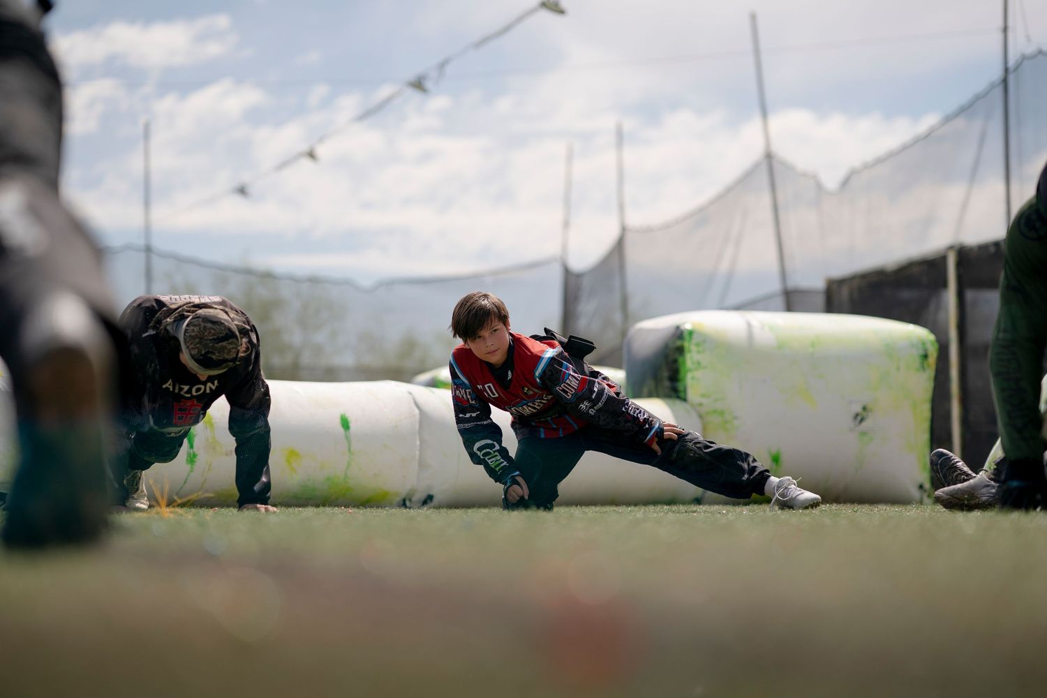 Paintball players take cover behind inflatable bunkers on an outdoor field with mountains in the background.
