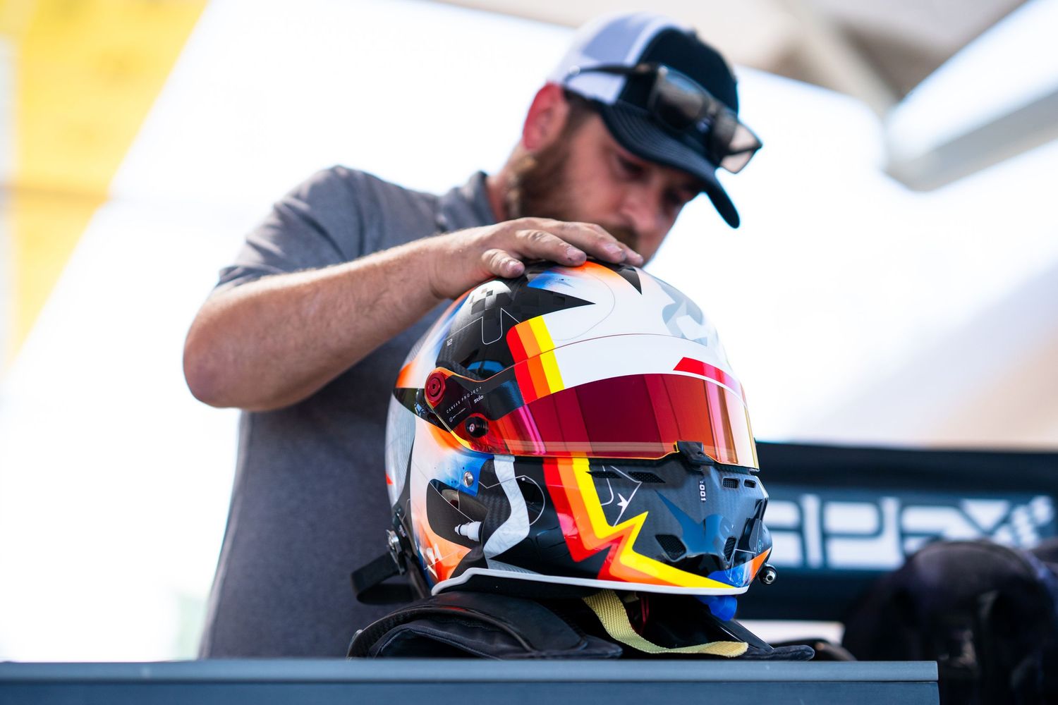 Racing driver in helmet preparing for competition in red Radical sports car cockpit.