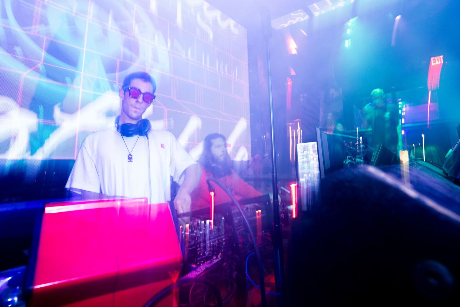 DJ performs at nightclub with colorful blue and pink lighting effects creating an energetic atmosphere.