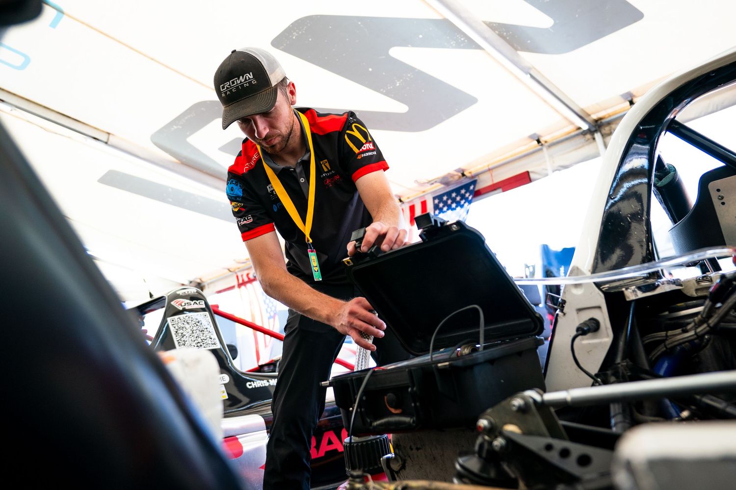 Racing team mechanics and engineers working on car setup adjustments in the garage.