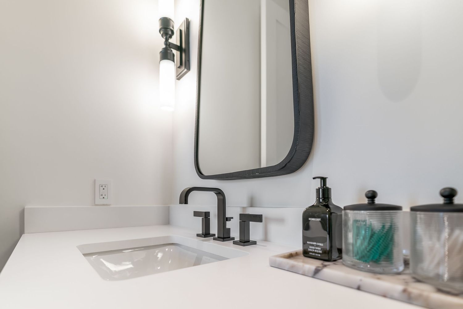 A modern bathroom interior with black fixtures, white walls, and a sleek mirror mounted above the sink.