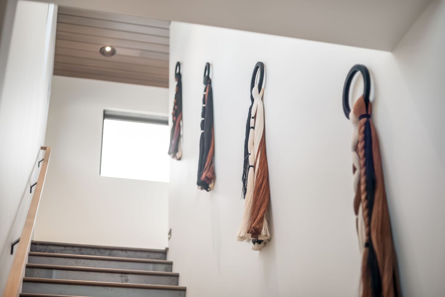 A brown leather handbag hangs on a white wall hook against a clean white wall with natural lighting.