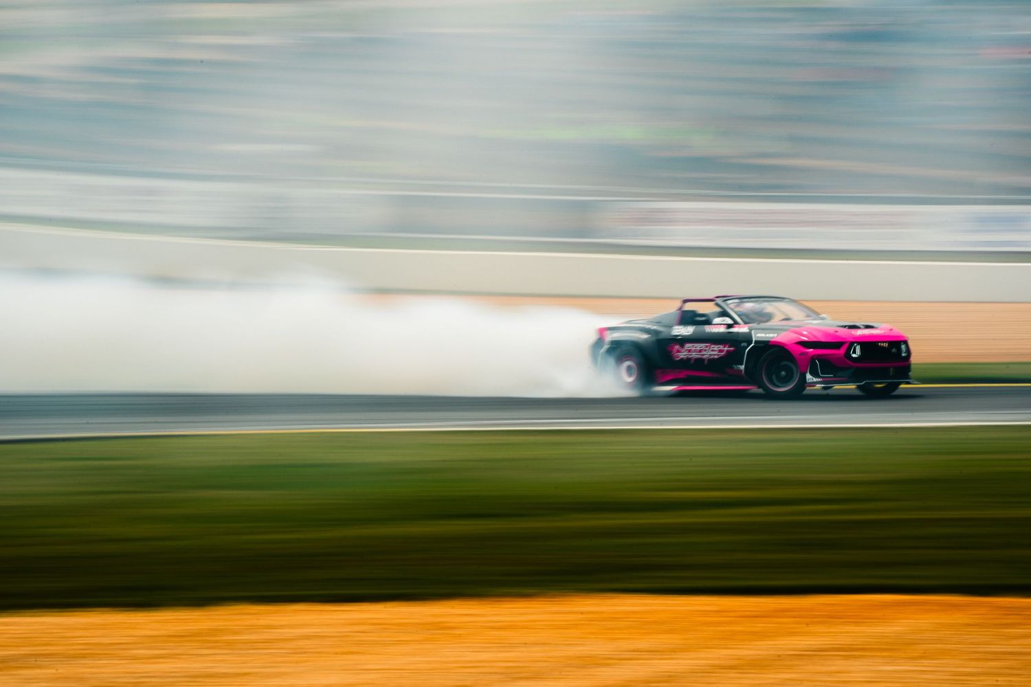 Pink convertible drift car sliding through smoke on a race track at high speed.